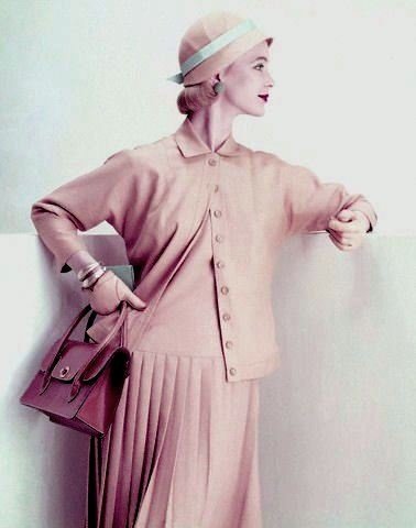 1955    Model is wearing an amber suit of linen rayon, a long torso jumper with a knife pleated skirt and a hip long jacket by Majestic.