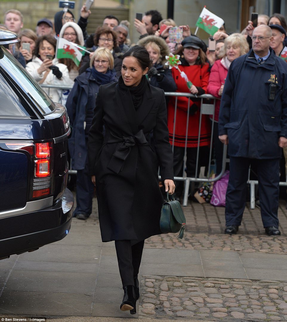 Meghan stepped out of her car in a long black coat tied with a silk ribbon sash around the waist and velvet boots 
